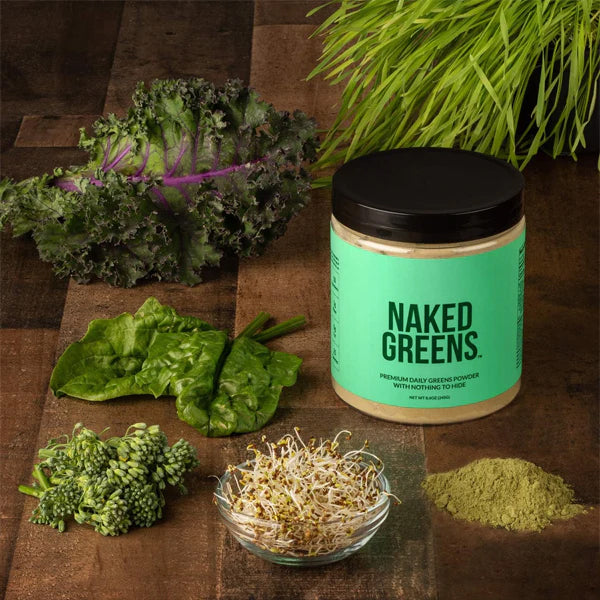 A jar of Naked Nutrition’s Naked Super Greens Powder Organic Greens Supplement 8.6oz sits on a wooden surface, surrounded by leafy greens, sprouts, and green powder—highlighting this organic supplement in a fresh setting.